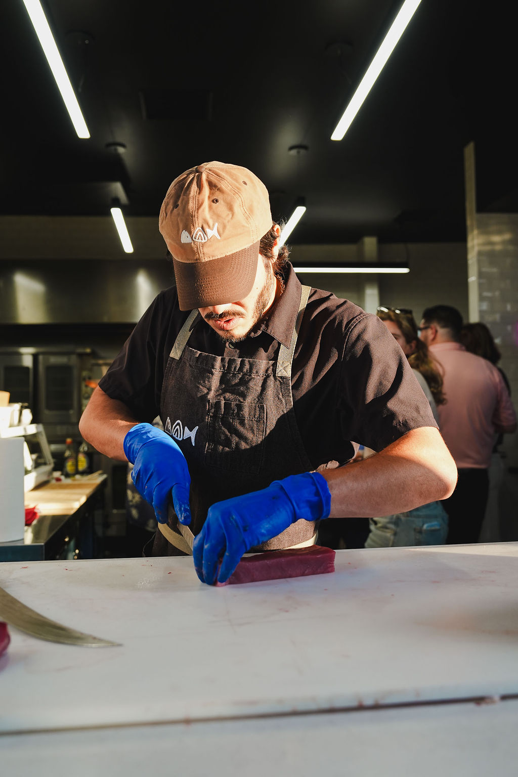 Blake Ito slicing a block of akami at the board, guests watching behind him.